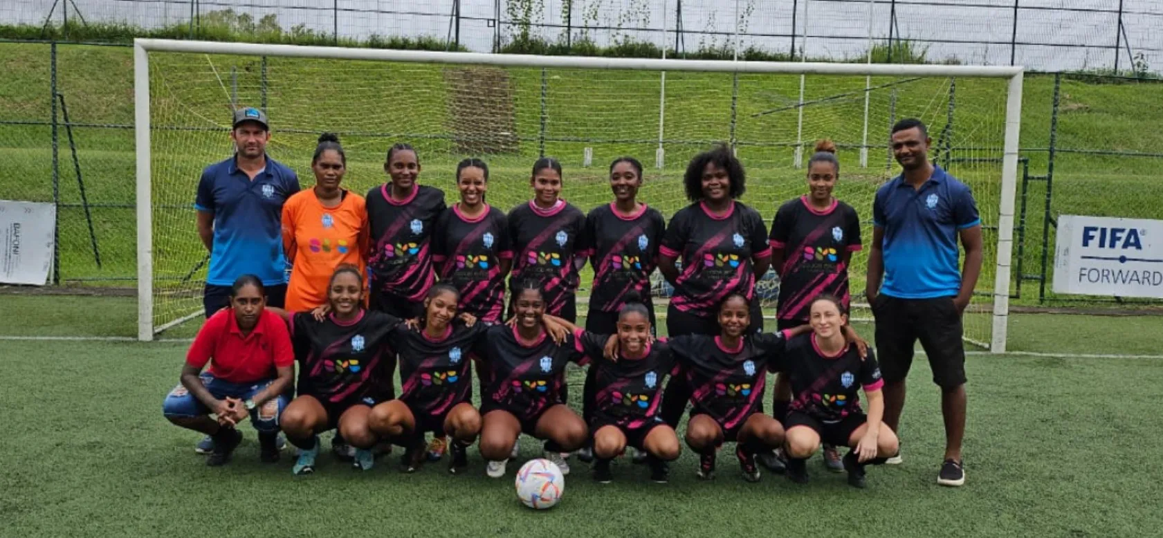 Pointe aux Piments Fire City women's football team posing in black and pink kits with coaches in front of a goal